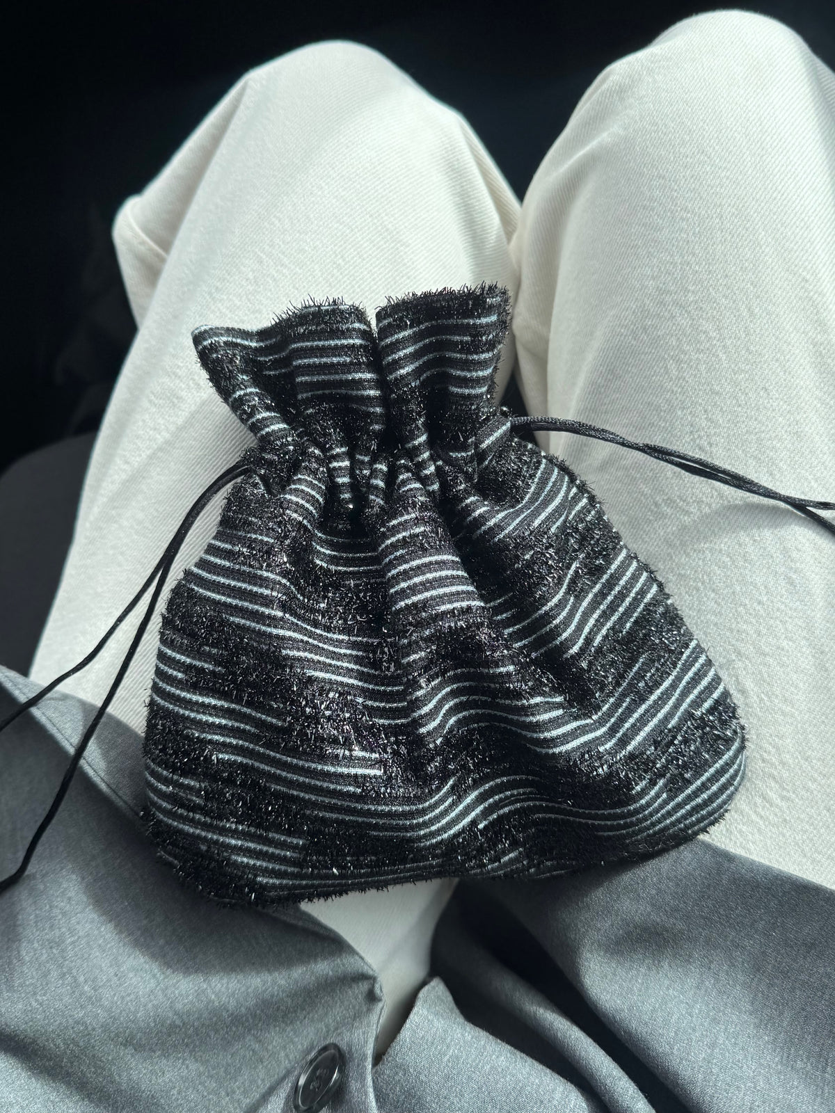 A small black and white striped drawstring pouch resting on a person's lap, with white pants and a gray top visible in the background.