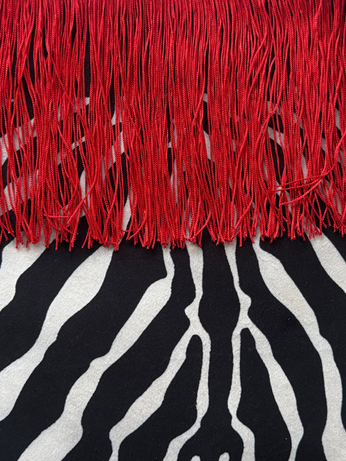 A close-up of a textile product showing bright red fringe across the top and a black-and-white zebra print below.