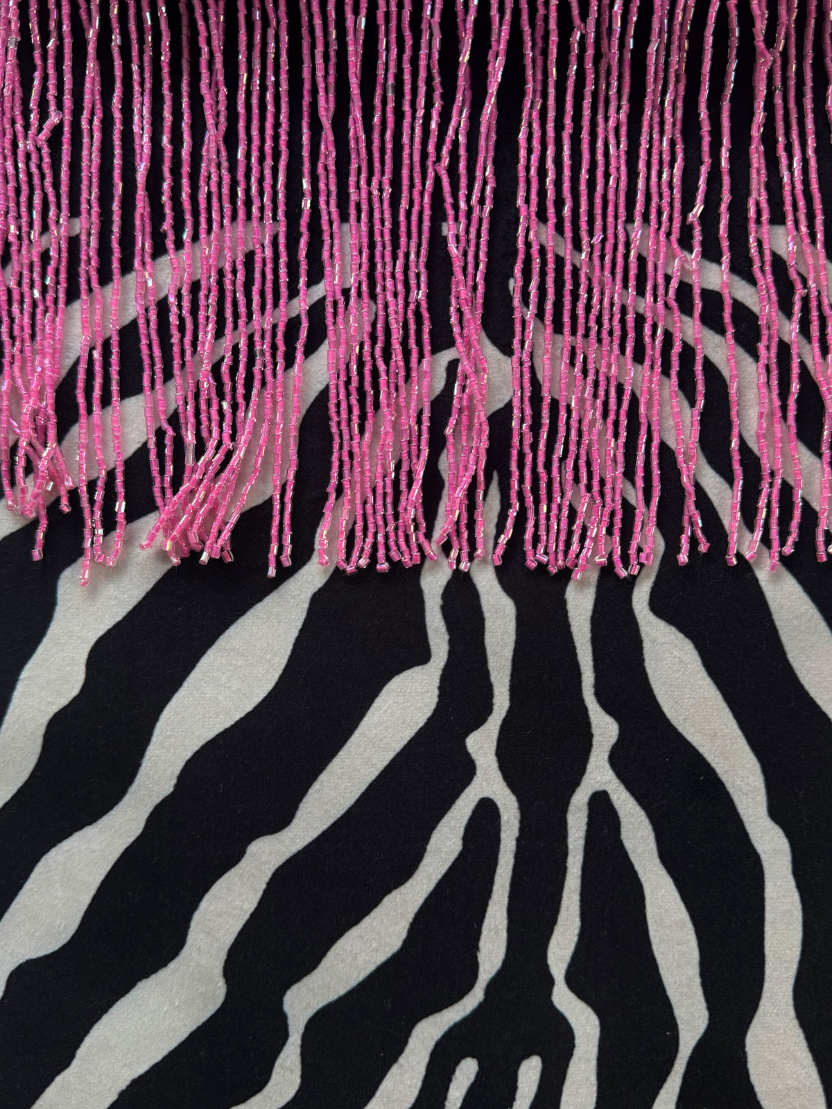 A close-up of a textile featuring bright pink fringe across the top and a black-and-white zebra print below.